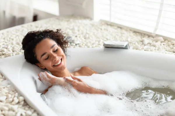 Mandi santai. Wanita muda yang bahagia berbaring di bak mandi dengan mata tertutup, menikmati ritual kecantikan di spa mewah, menyalin ruang — Stok Foto
