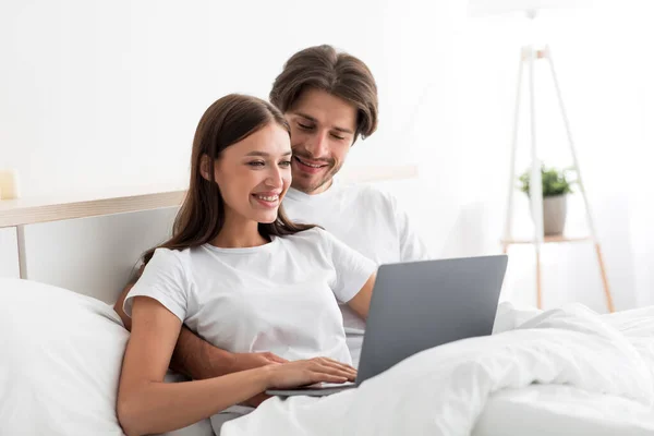 Щаслива красива тисячолітня біла дама і хлопець дивляться на ноутбук балачки або роблять відеодзвінок на ліжко — стокове фото