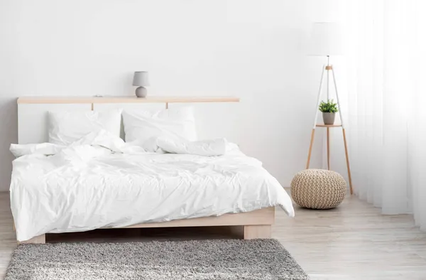 Komfortowe podwójne łóżko, lampa, miękki szary dywan, meble z akcesoriami, okno z zasłonami — Zdjęcie stockowe