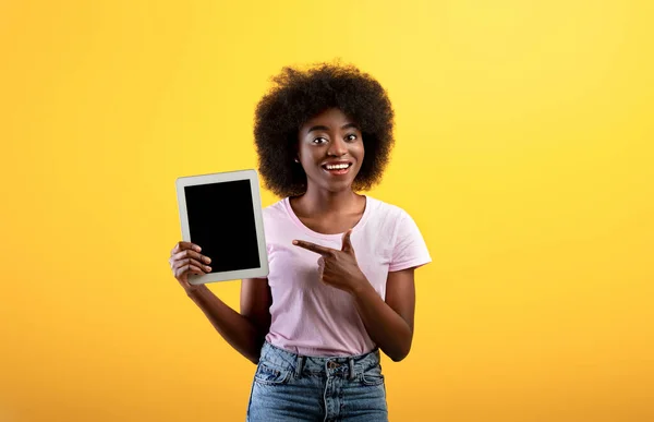 Happy african american lady pointing at digital tablet with blank screen, yellow background, mockup — Stock Photo, Image
