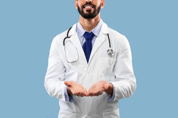 Médecin masculin arabe méconnaissable montrant un objet invisible sur fond bleu — Photo
