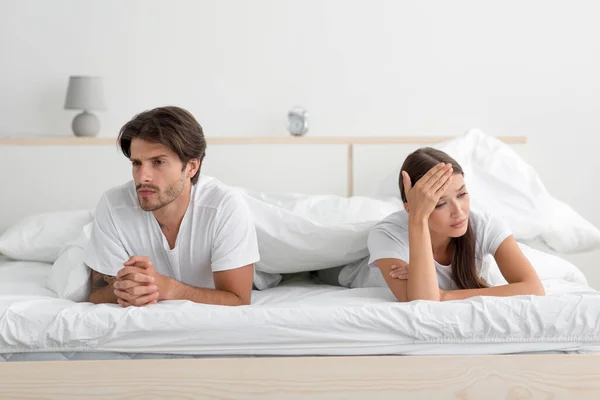 Ofendida joven pareja caucásica enojada acostada en la cama ignorando a su pareja en el dormitorio —  Fotos de Stock
