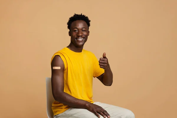 Концепция вакцинации. Счастливый привитый чернокожий парень стреляет пальцем в камеру — стоковое фото