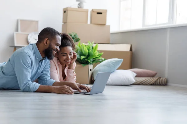 Sorrindo millennial afro-americano masculino e feminino encontra-se no chão em novo apartamento entre caixas, planejando interior — Fotografia de Stock