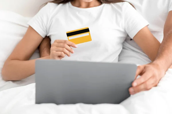 Fehér Y-generációs férfi ölelés nő, hölgy birtokol hitelkártya és megrendelések áruk laptop, ülni az ágyban, kivágott — Stock Fotó