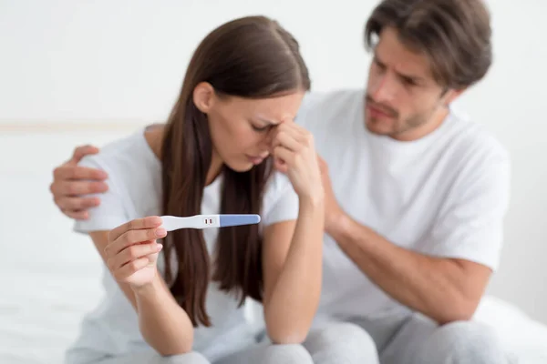 Despaired sad millennial european husband calms, support his wife, lady hold pregnancy test — Stock Photo, Image