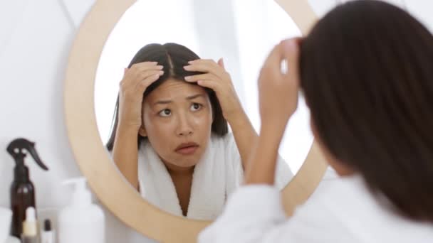 Проблема с перхоти. Молодая эмоциональная женщина в халате смотрит в зеркало и с ужасом осматривает свои грязные волосы — стоковое видео