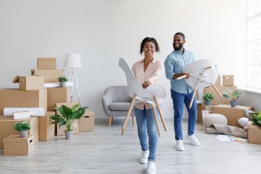 Mutlu genç siyah adam ve kadın yeni evlerinde kutularla sandalyeler taşıyorlar. Bir çift mobilya yerleştiriyor, yeni bir daireye taşınıyor.