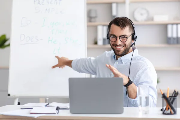 Amistoso adulto europeo hombre profesor en gafas muestra a bordo con reglas, mira el portátil webcam — Foto de Stock