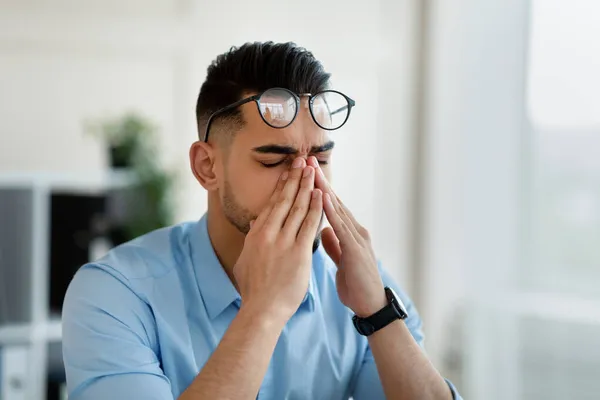 Fiatal arab irodai munkás szemüvegben dörzsöli fáradt szemét, kimerült a modern irodai munkától, másolja a helyet — Stock Fotó