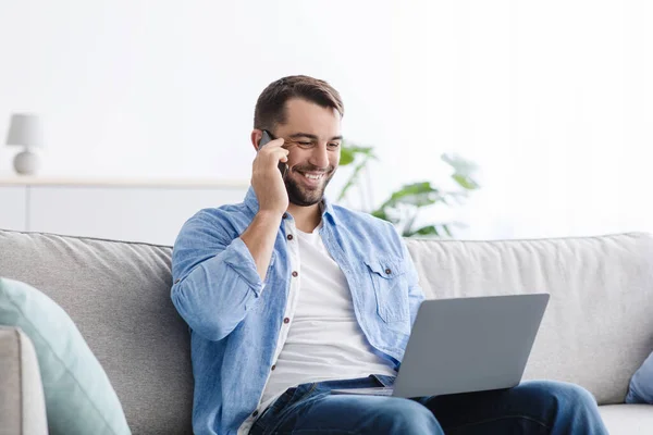 Alegre guapo adulto europeo chico han llamado con el cliente, trabajando en el ordenador portátil en el interior de la sala de estar — Foto de Stock