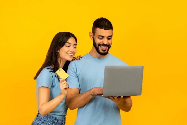 Concepto de compras online. Feliz pareja árabe joven usando computadora portátil, dama con tarjeta de crédito de débito dorado — Foto de Stock
