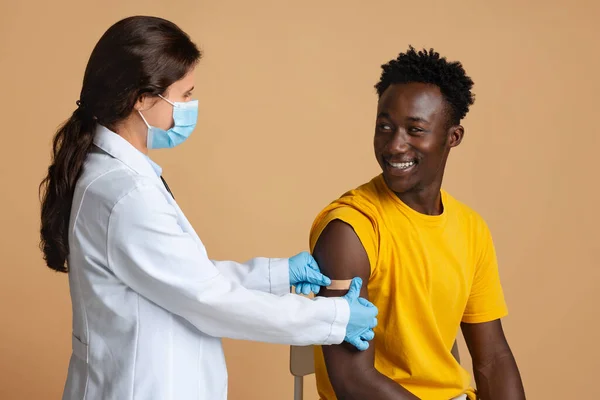 Después de la vacunación. Alegre hombre negro consiguió vacunado contra el Coronavirus, Enfermera Aplicando vendaje —  Fotos de Stock