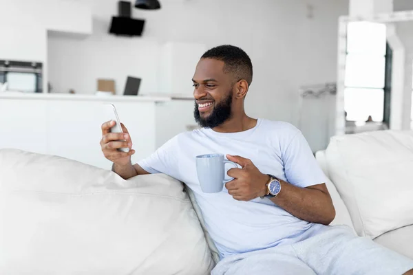 Negro chico mensajes de texto en su teléfono inteligente beber café — Foto de Stock