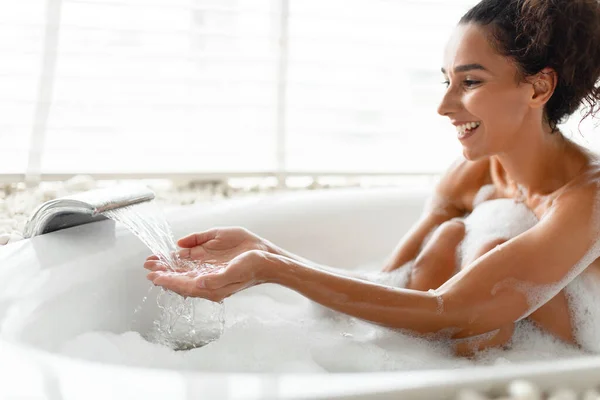 Sexy młoda kobieta biorąc kąpiel z bąbelkami, uczucie bieżącej wody z kranu, co do domu zabieg spa, przestrzeń kopiowania — Zdjęcie stockowe