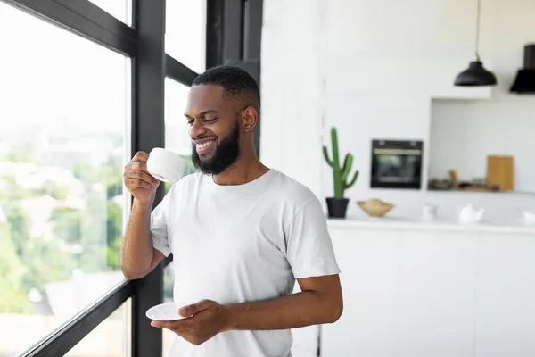 창문 근처에서 커피를 마시고 있는 아프리카 계 미국인의 웃는 모습 — 스톡 사진