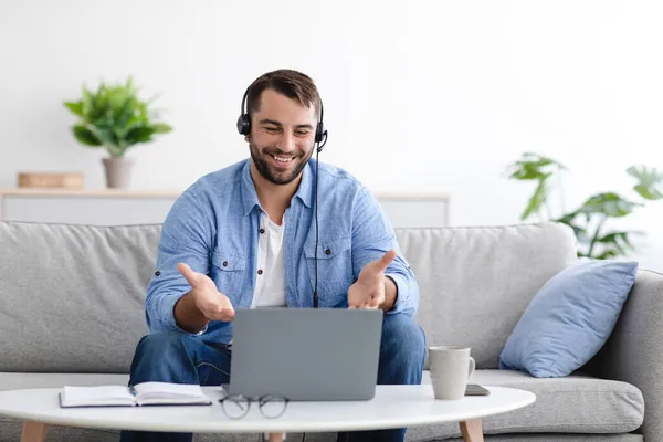 Счастливый взрослый европейский мужчина в наушниках имеет видео-звонок на ноутбуке в гостиной интерьер — стоковое фото