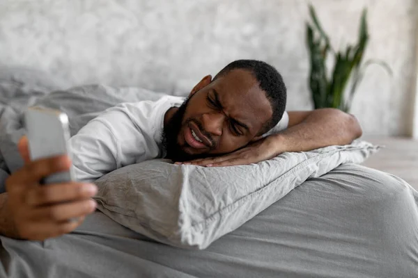 睡眠不足的黑人躺在床上看手机 — 图库照片