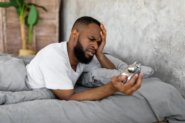Hombre negro que sufre de insomnio mirando el reloj en la cama — Foto de Stock