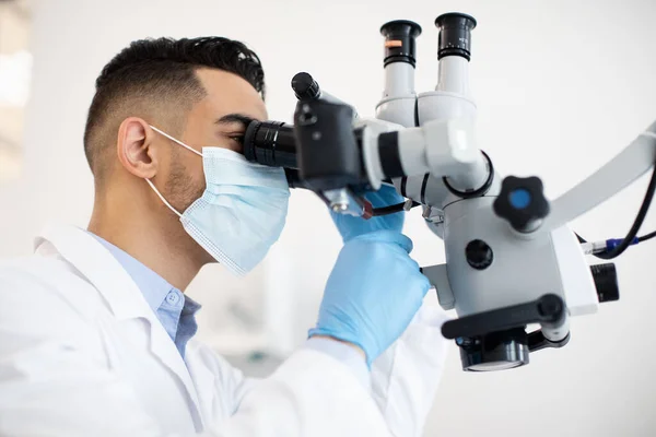 Joven médico estomatólogo árabe investigando con microscopio dental — Foto de Stock