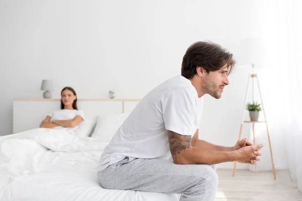 Triste ofendido raiva jovem caucasiano marido sentado na cama, ignorando a esposa com os braços cruzados no quarto — Fotografia de Stock