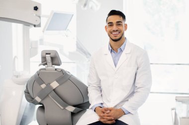 Gülümseyen Orta Doğulu Erkek Diş Hekimi Modern Klinikte İşyerinde Oturuyor