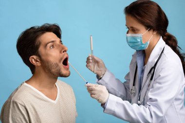 Bayan hemşire elinde pamuklu çubuk tutarak Oral PCR Coronavirus Testi yapıyor.