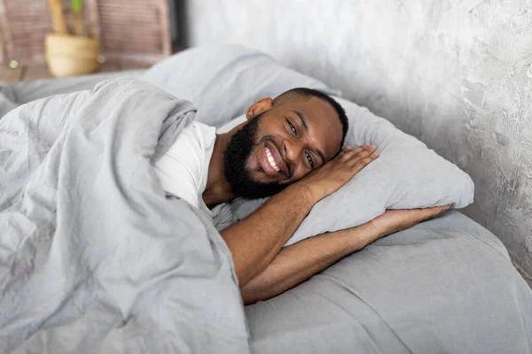 Νεαρός Αφροαμερικανός ξαπλωμένος στο κρεβάτι κοιτάζοντας την κάμερα — Φωτογραφία Αρχείου
