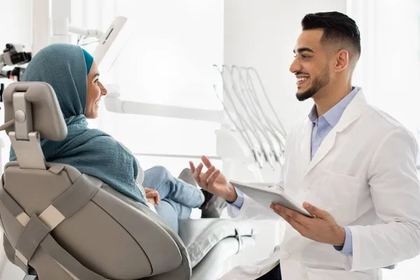 Zahnarzt mit digitalem Tablet in der Hand berät muslimische Patientin in Klinik — Stockfoto