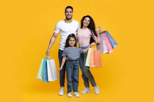 Ventas estacionales. Familia árabe feliz con la pequeña hija sosteniendo brillantes bolsas de compras —  Fotos de Stock