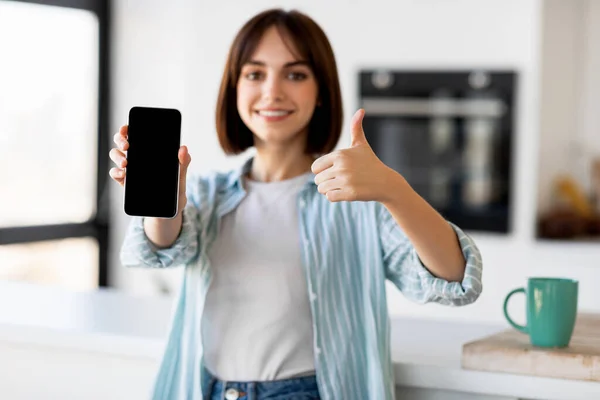 Felice giovane signora che tiene smartphone con schermo bianco e mostrando pollice in su, raccomandando app per la consegna del cibo — Foto Stock