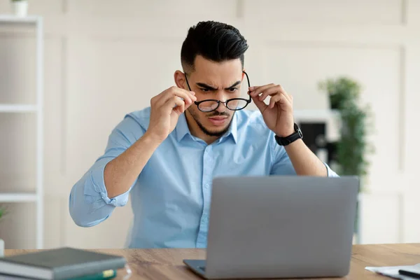 Ερεθισμένος Άραβας επιχειρηματίας που κοιτάζει την οθόνη του φορητού υπολογιστή, έχοντας πρόβλημα στην online εργασία στο γραφείο — Φωτογραφία Αρχείου