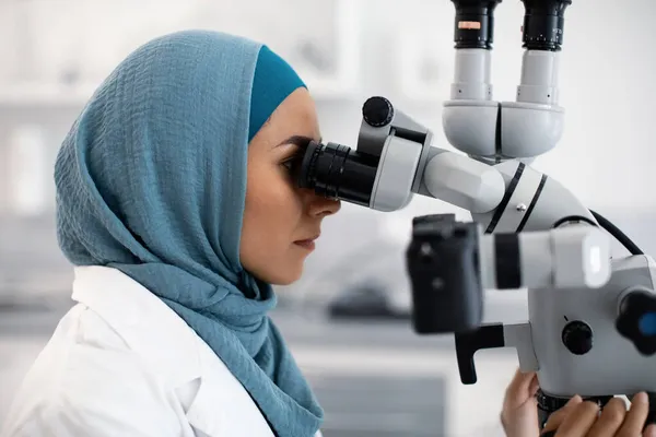 Medico dentista femminile musulmana che utilizza il microscopio dentale sul posto di lavoro nella clinica moderna — Foto Stock