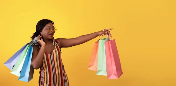 陽気な黒の女性でドレスを保持ショッピングバッグ、脇に指しています空のスペース上のオレンジスタジオの背景 — ストック写真