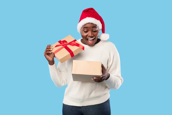 Czarna Pani Otwieranie Boże Narodzenie prezent na sobie Santa kapelusz, niebieskie tło — Zdjęcie stockowe