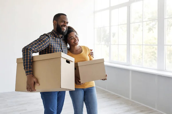 Feliz sorriso milenar casal afro-americano carrega caixas de papelão com pertences, abraçando — Fotografia de Stock