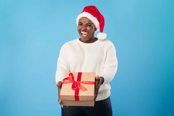 Radosna Afroamerykanka daje prezent świąteczny do kamery, niebieskie tło — Zdjęcie stockowe