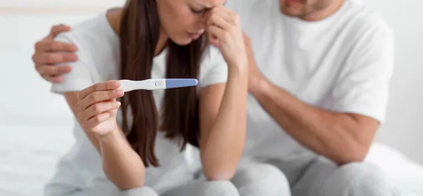Przycięte rozczarowany młody biały mężczyzna wspierać jego żona, trzymać test ciążowy, siedzieć na łóżku w sypialni — Zdjęcie stockowe