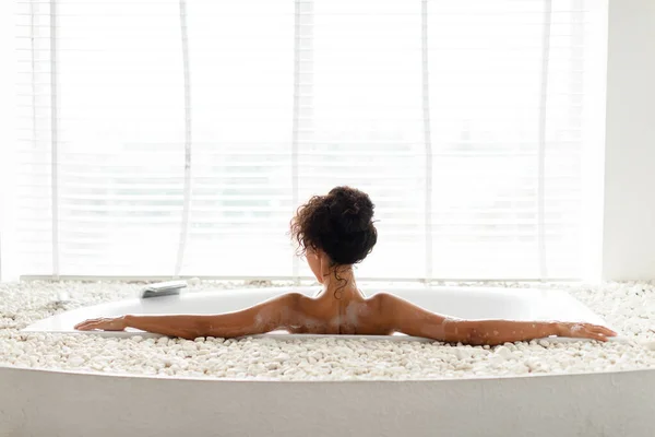 Πίσω όψη της χιλιετίας γυναίκα λαμβάνοντας αφρώδες μπάνιο, κοιτάζοντας έξω από το παράθυρο στο σπίτι, κενό χώρο — Φωτογραφία Αρχείου