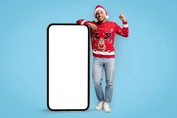 Geïnspireerd zwarte man in Santa hoed staan door enorme mobiele telefoon — Stockfoto
