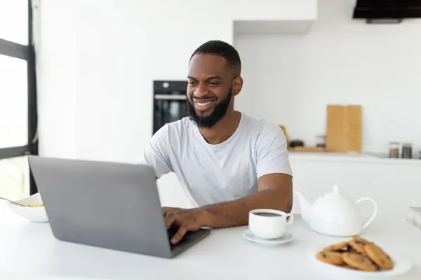 Αφροαμερικανός που χρησιμοποιεί φορητό υπολογιστή στην κουζίνα — Φωτογραφία Αρχείου