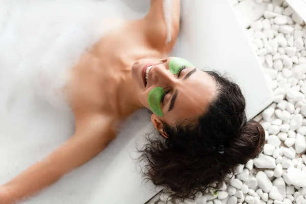 Sensual joven acostada en baño de burbujas con parches para los ojos, vista superior —  Fotos de Stock