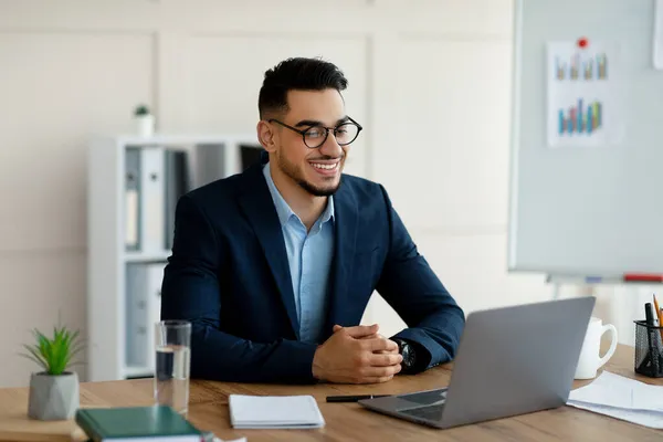 Αυτοπεποίθηση νεαρός Άραβας επιχειρηματίας με επίσημο κοστούμι χρησιμοποιώντας φορητό υπολογιστή στο γραφείο του, έχοντας εικονική συνάντηση στο γραφείο — Φωτογραφία Αρχείου