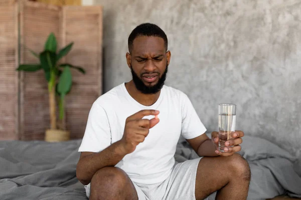 Homme noir prenant des pilules tenant un verre d'eau — Photo