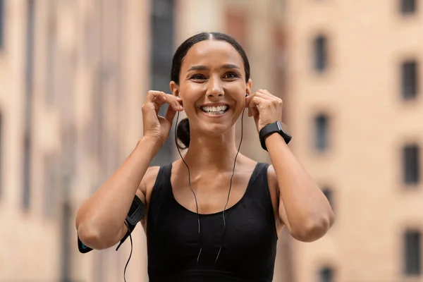 Playlist de exercícios. Feliz jovem atlético senhora colocando em fones de ouvido antes de correr ao ar livre — Fotografia de Stock