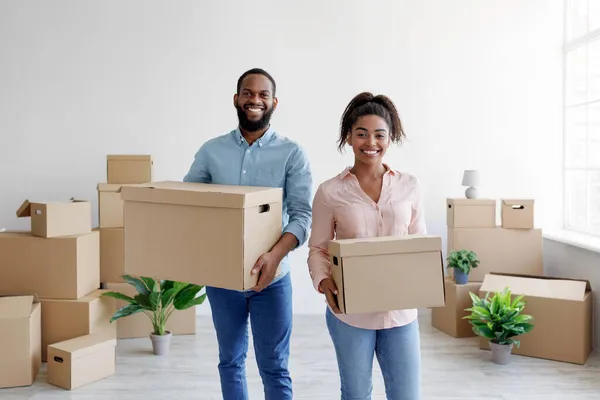 Ικανοποιημένοι νέοι αφροαμερικάνοι σύζυγοι μεταφέρουν κουτιά με αντικείμενα σε νέο διαμέρισμα. — Φωτογραφία Αρχείου
