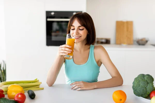 Avgiftningsdiet. Smal dam dricka apelsinjuice medan matlagning hälsosam grönsak middag, sitter i ljus modernt kök — Stockfoto