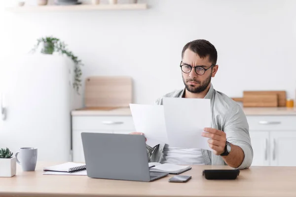 Concentré occupé homme caucasien mature dans des lunettes de travail avec des documents près d'un ordinateur portable — Photo