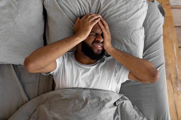 Hombre negro que sufre de dolor de cabeza o migraña en la cama — Foto de Stock
