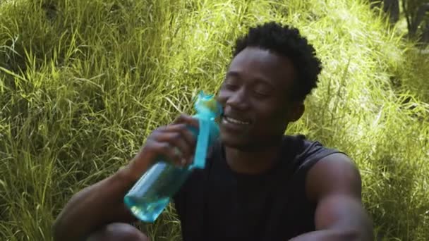 Homem africano vestindo roupas esportivas água potável de garrafa de esporte ao ar livre — Vídeo de Stock